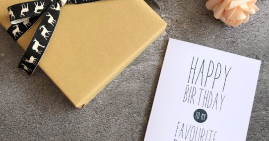 Birthday card reading happy birthday to my favourite person next to a wrapped gift and pink roses