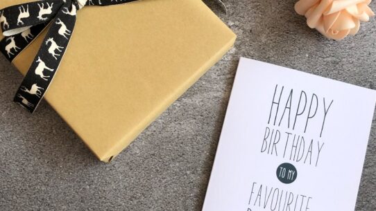 Birthday card reading happy birthday to my favourite person next to a wrapped gift and pink roses