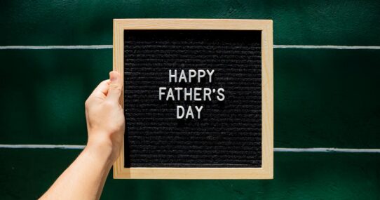 Happy Father's Day letter board in wooden frame held against green wall