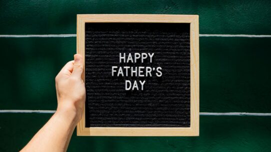 Happy Father's Day letter board in wooden frame held against green wall