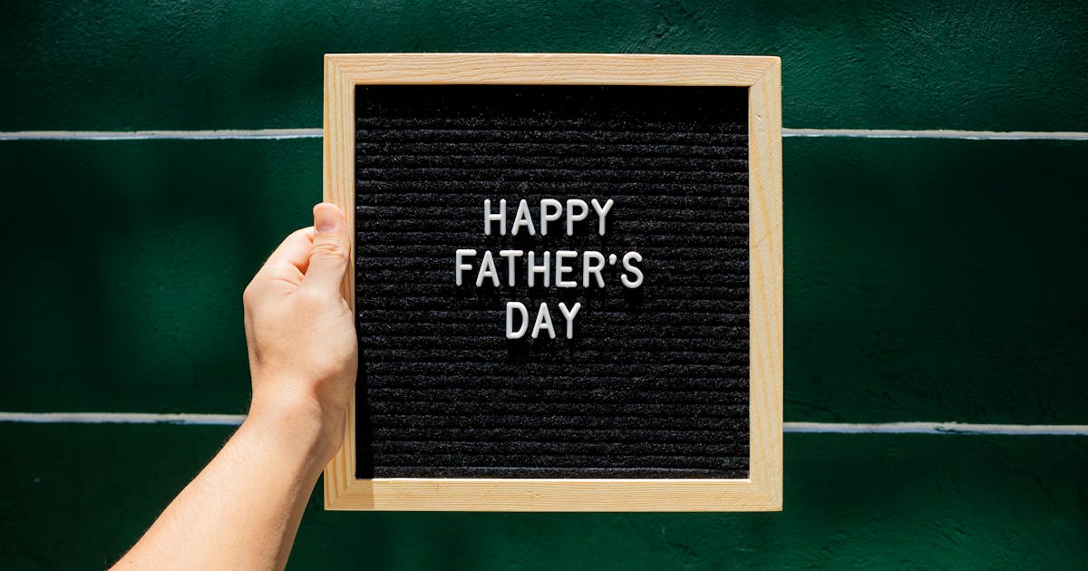 Happy Father's Day letter board in wooden frame held against green wall